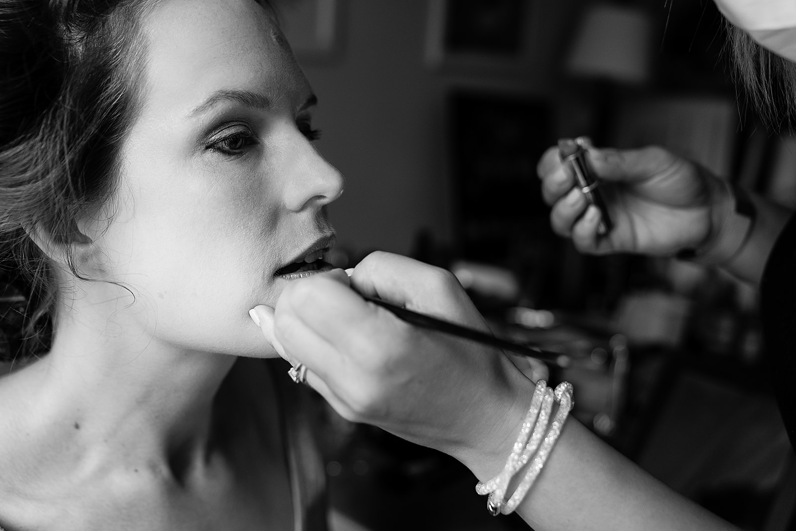 a black and white photo of a brdie having her lipstick applied by the hand of a MUA