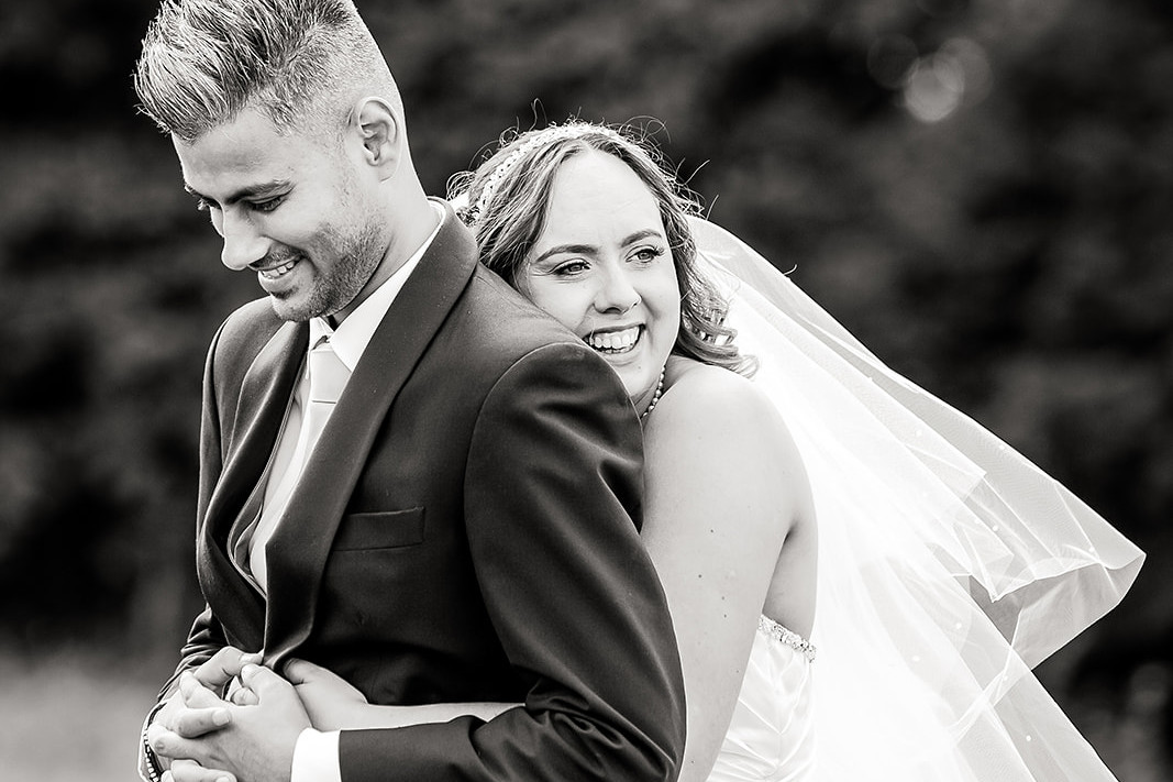 a black and white image of a bride hugging her groom from behind, both smiling